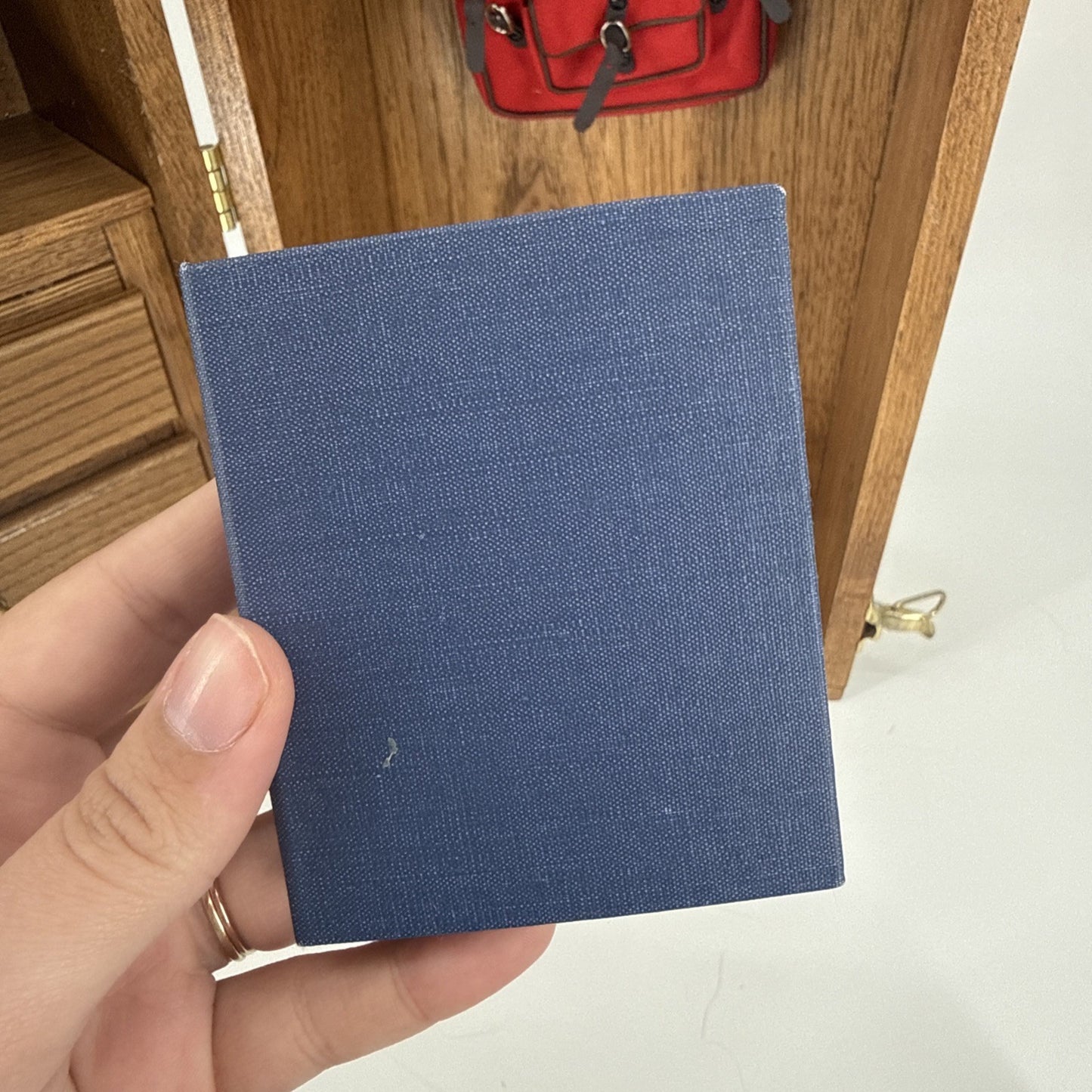 Hand holding a blue fabric sample in front of a wooden cabinet with a red bag on top.