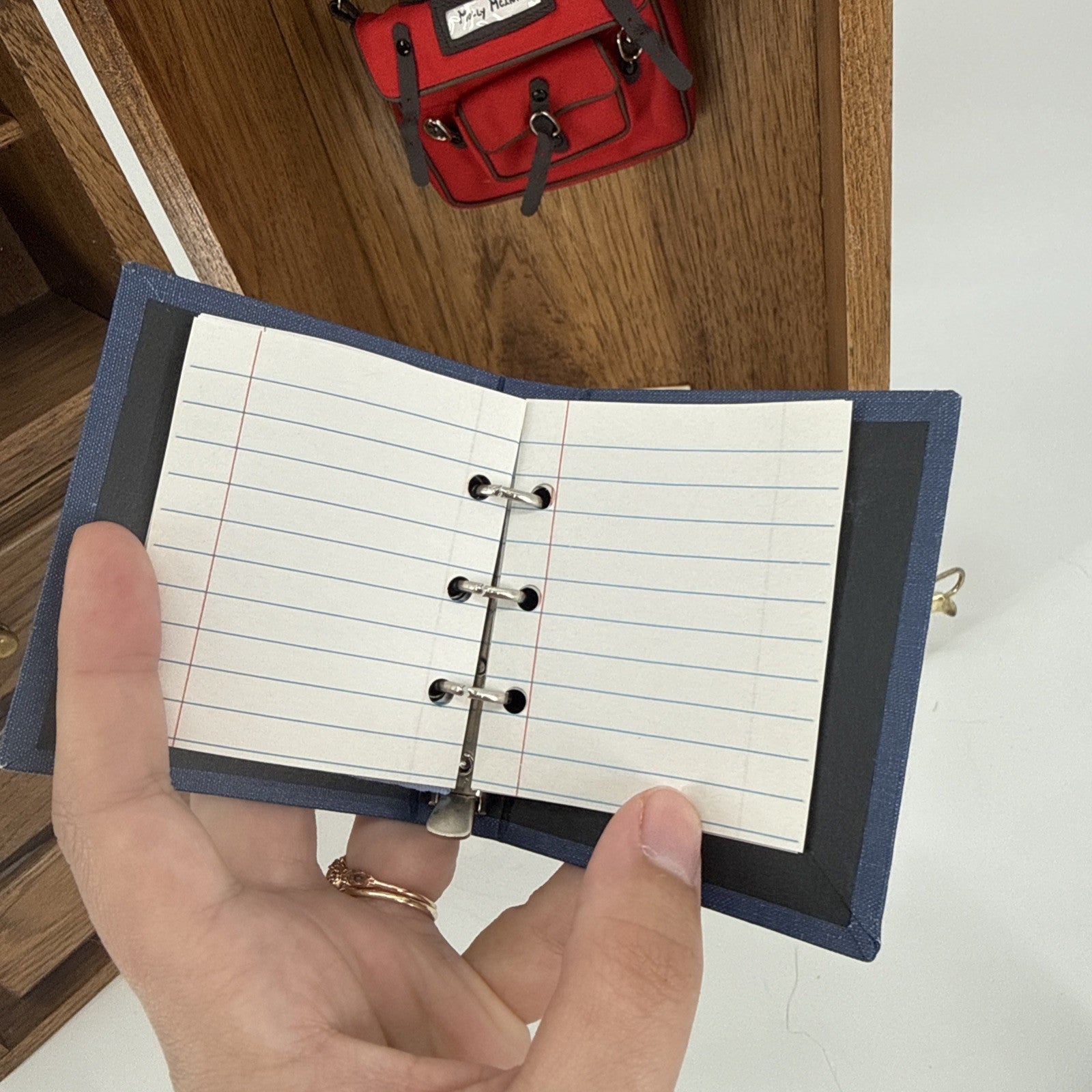 Hand holding a small open notebook with lined pages on a wooden surface.