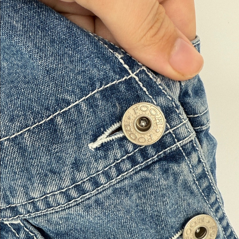 Close-up of a button on a blue denim jacket with a hand pressing it.