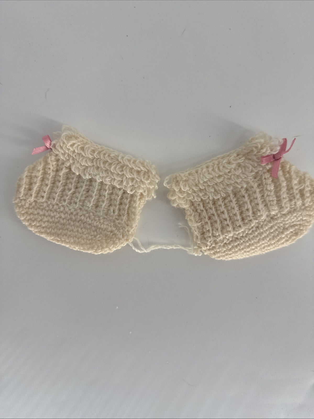 Pair of beige knitted baby booties with pink ribbons on a light gray background
