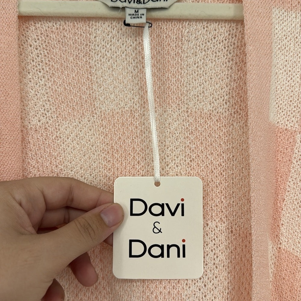 Hand holding a 'Davi & Dani' tag against a textured pink background