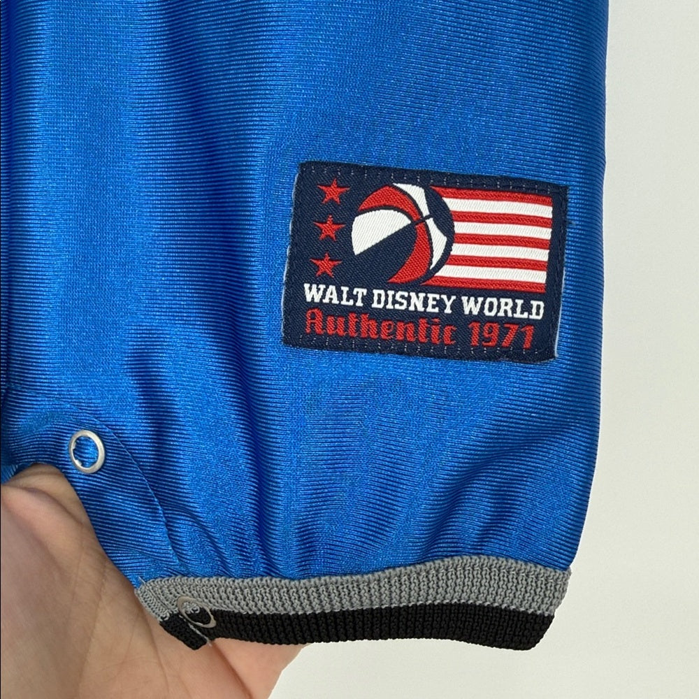 Close-up of Walt Disney World ‘Authentic 1971’ patch on blue Mickey Mouse basketball baby romper with gray trim and snap closure.