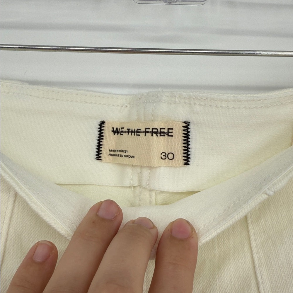 Close-up of a 'We the Free' label on a white garment with a hand for scale.