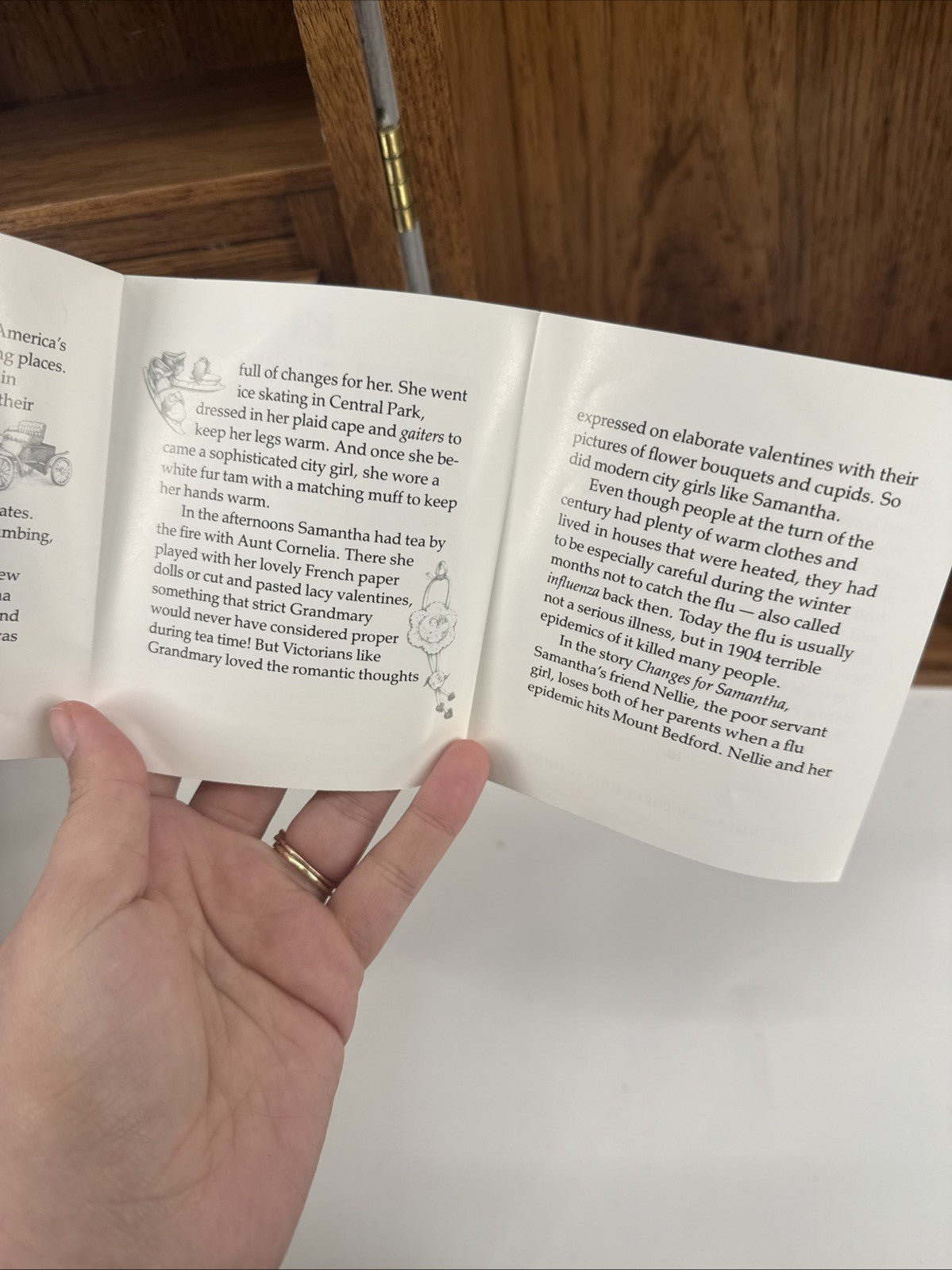 Hand holding an open book with text on a wooden surface