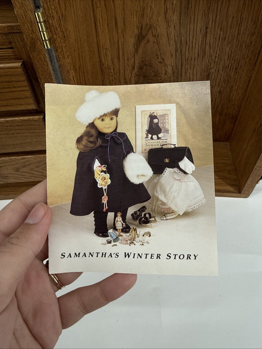 Hand holding a card with a winter-themed doll and accessories on a wooden surface.