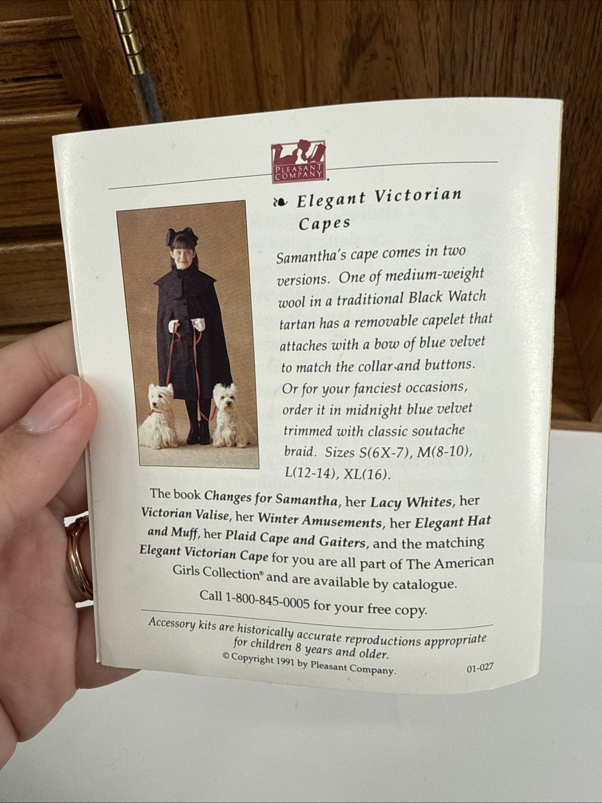 Hand holding a product description leaflet for 'Elegant Victorian Capes' with images of a person and dogs.