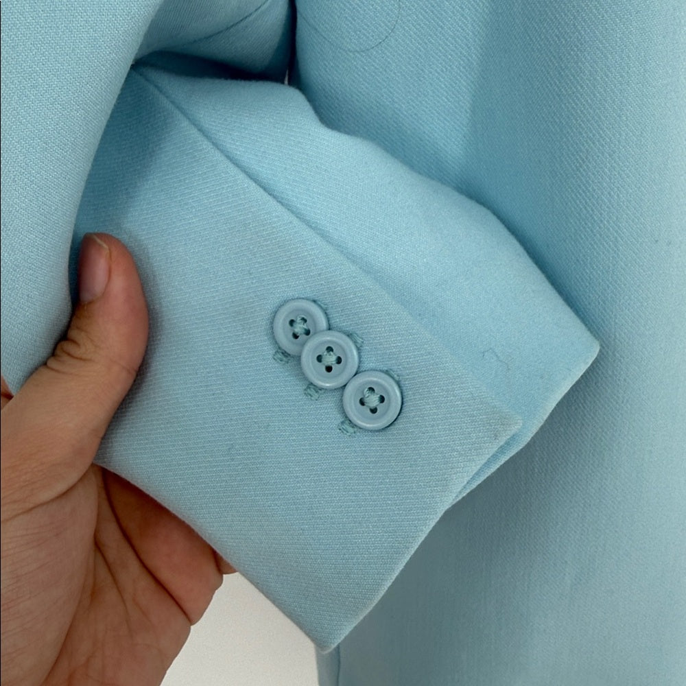 Light blue fabric with two buttons held by a hand against a matching background
