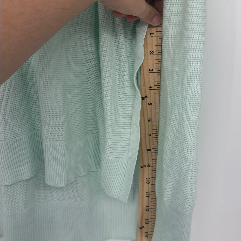 Light green sweater with a wooden ruler for size reference on a white background