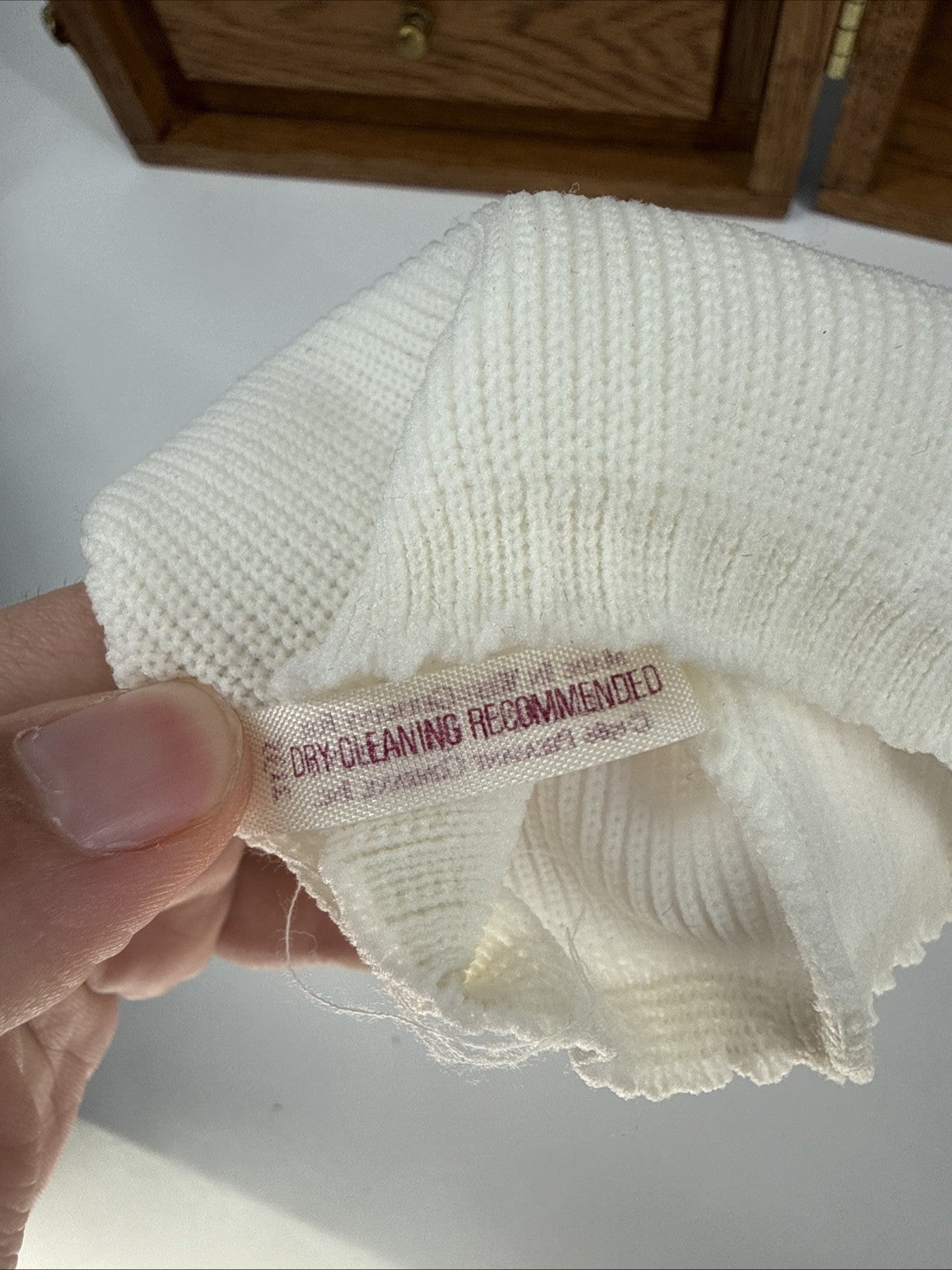 Close-up of a white fabric with a care label held by a hand on a light background