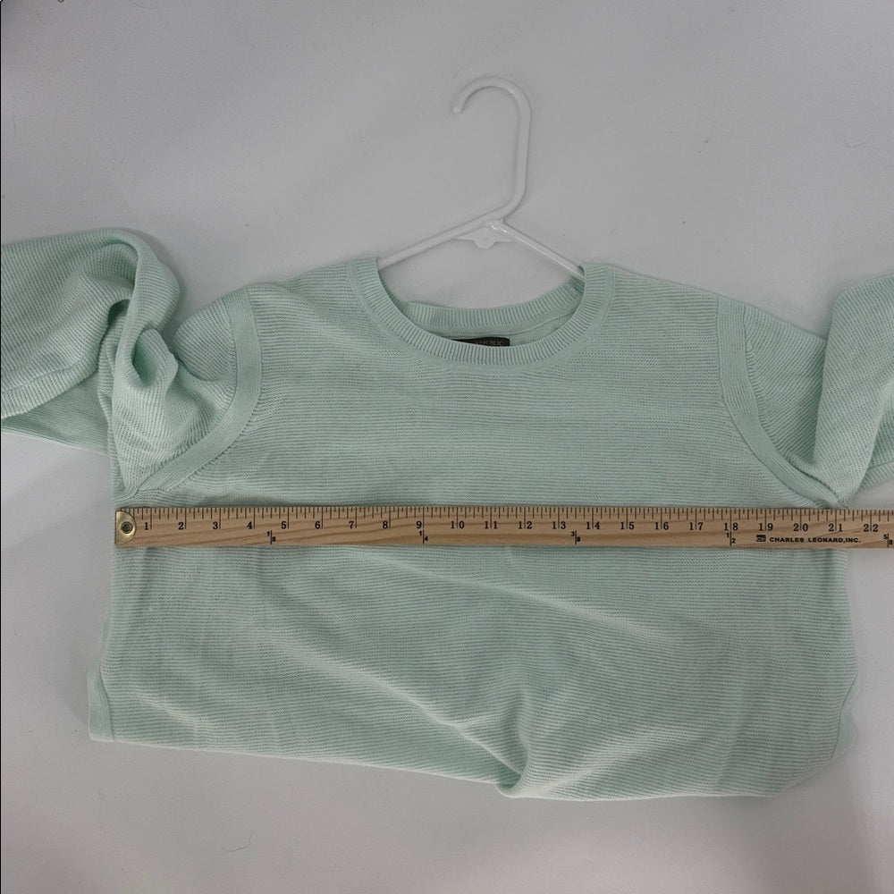 Light green crop top on a hanger with a ruler for size reference against a white background