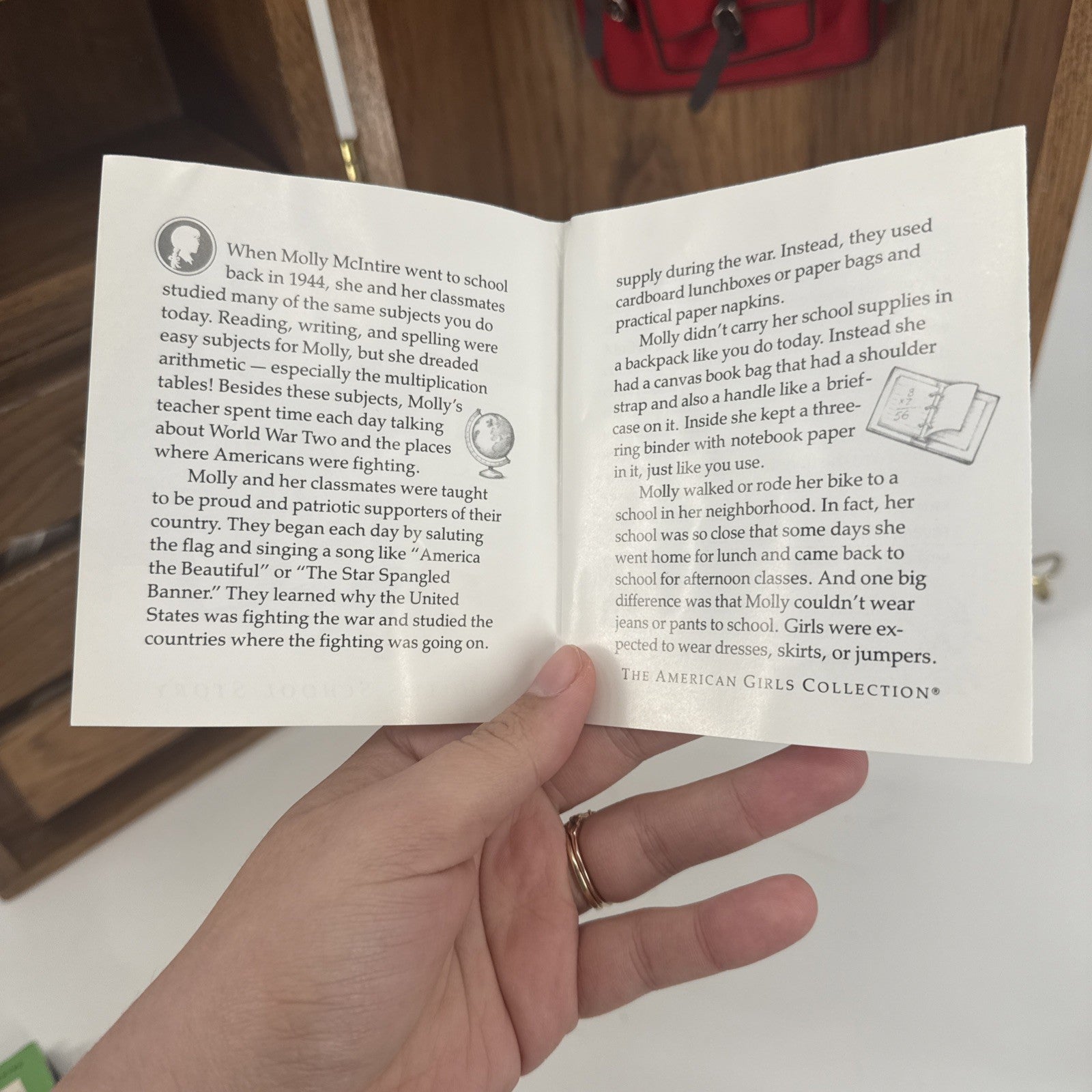 Hand holding an open book with text and illustrations on a wooden surface.
