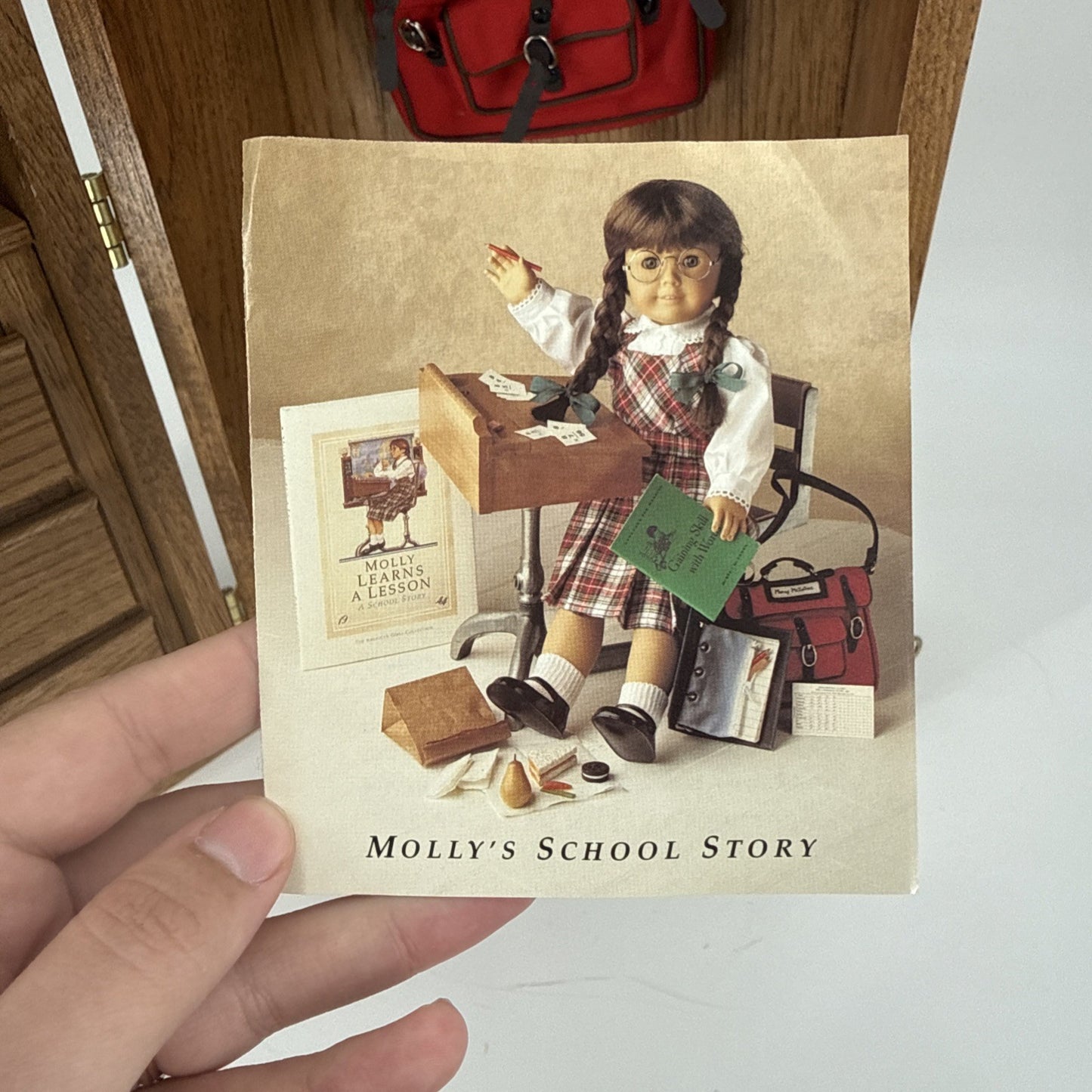 Book titled 'Molly's School Story' held by a hand with a wooden surface and red bag in the background.