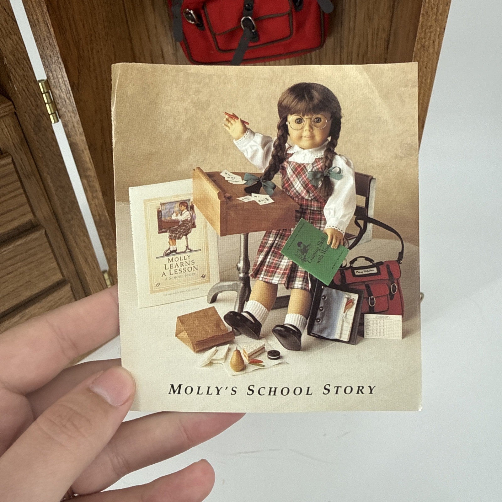 Book titled 'Molly's School Story' held by a hand with a wooden surface and red bag in the background.