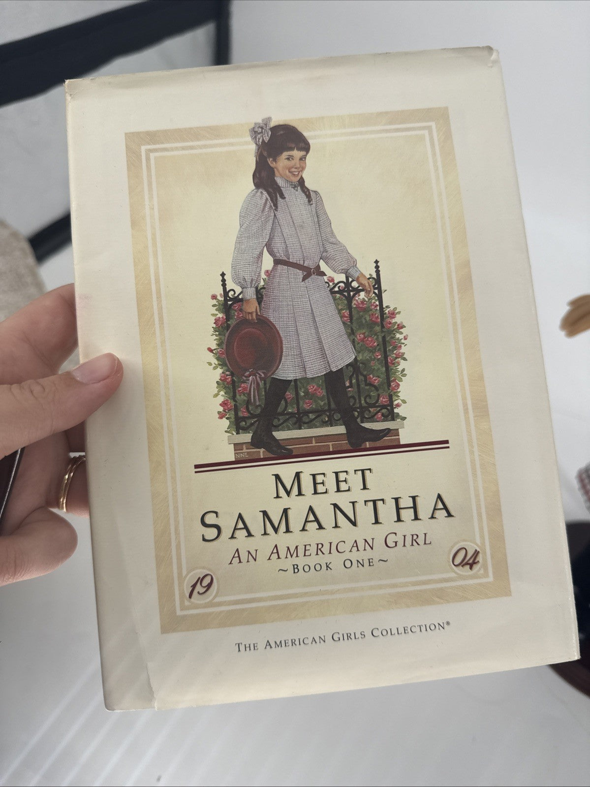 Book titled 'Meet Samantha: An American Girl' held by a hand on a white surface.