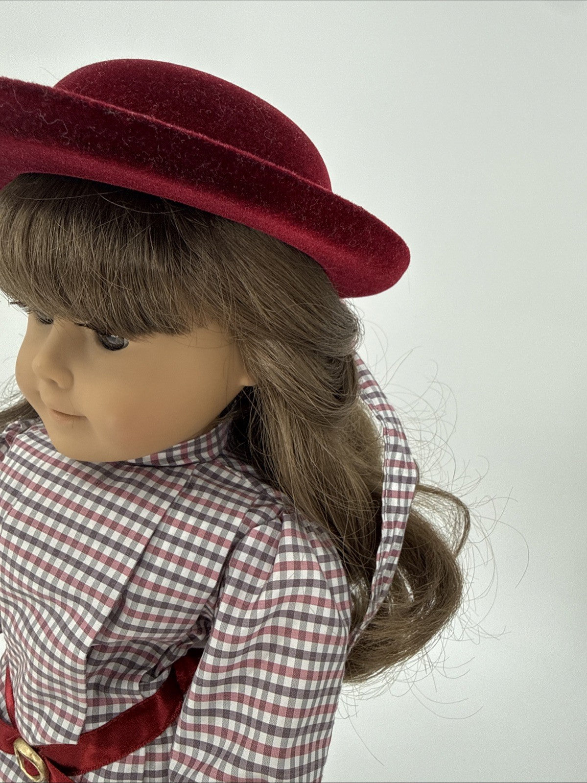 Doll wearing a red hat and checkered outfit on a plain background