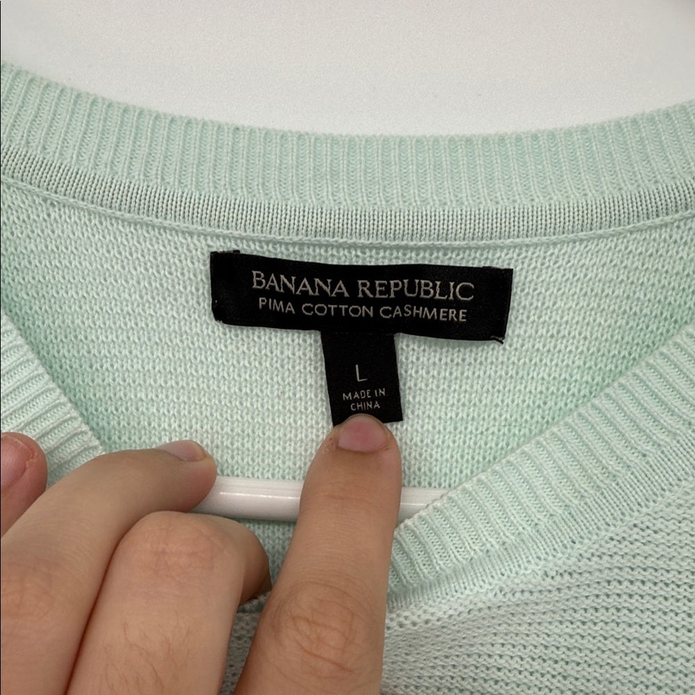 Close-up of a Banana Republic label on a light green sweater with a hand holding a pen.