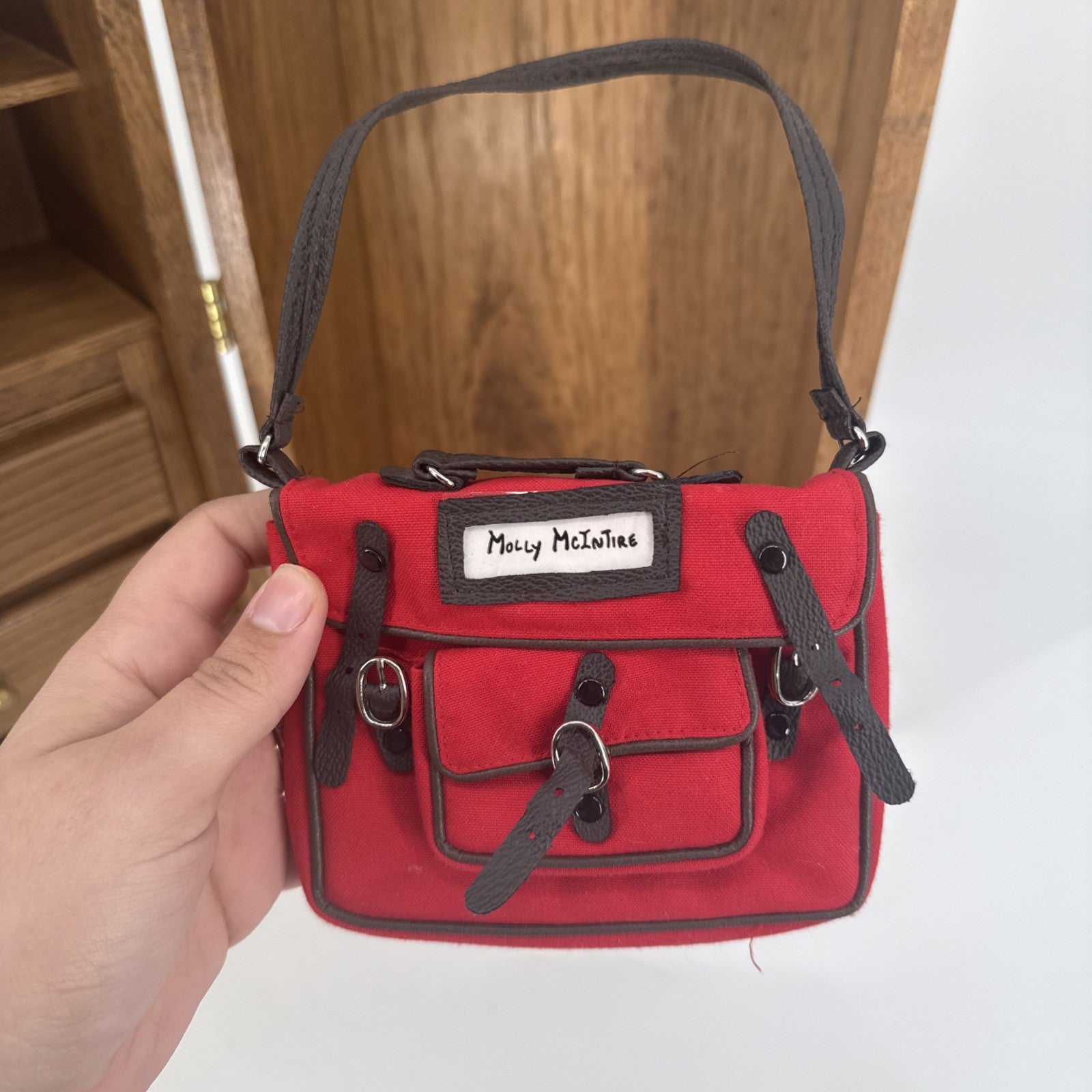 Red handbag with black straps held by a hand against a wooden background