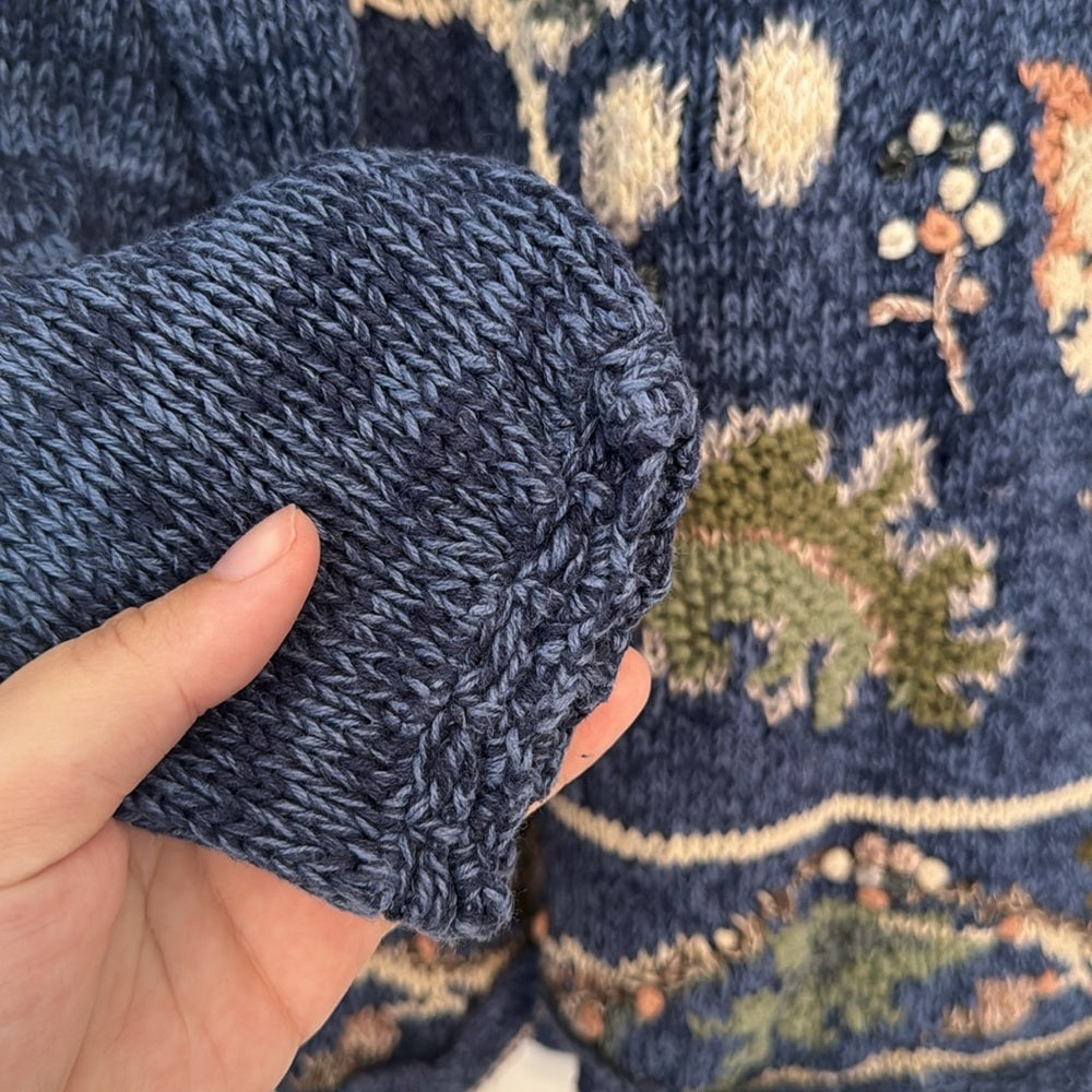 Sleeve of Blue knit sweater with an allover floral and botanical pattern, long sleeves, and ribbed hem.