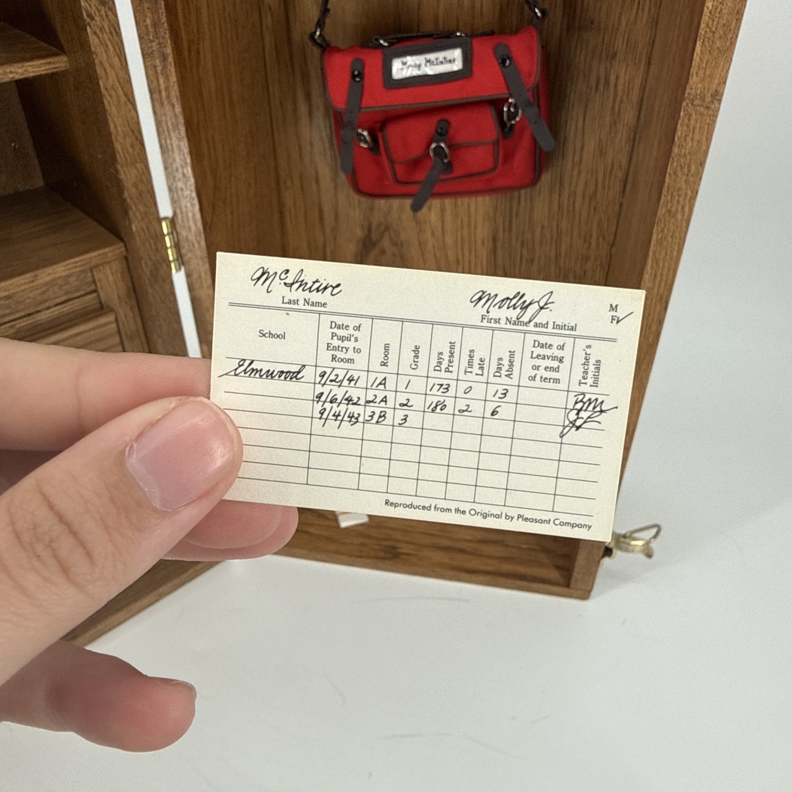 Hand holding a miniature school record card with a red bag in the background