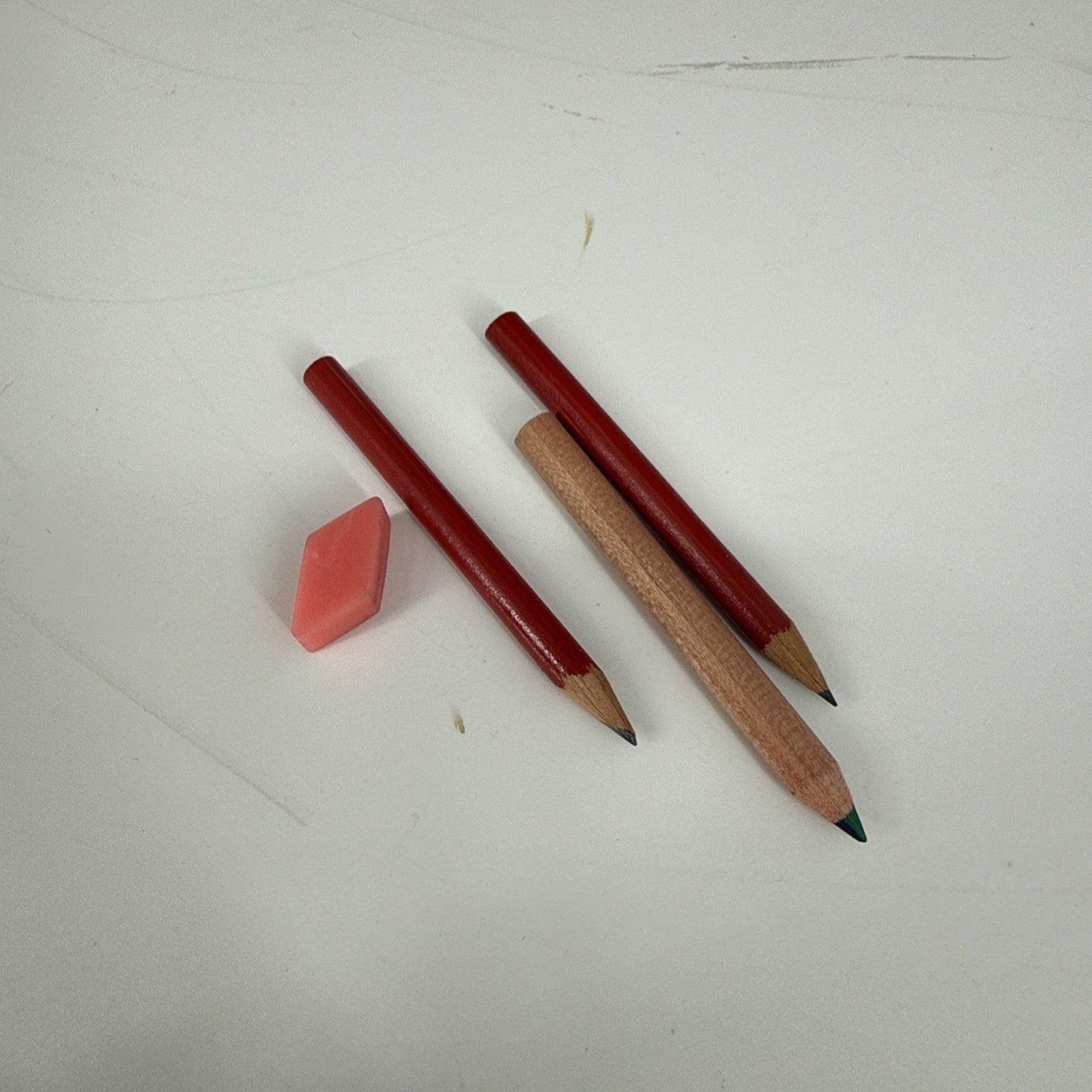 Two red pencils and a pink eraser on a white surface