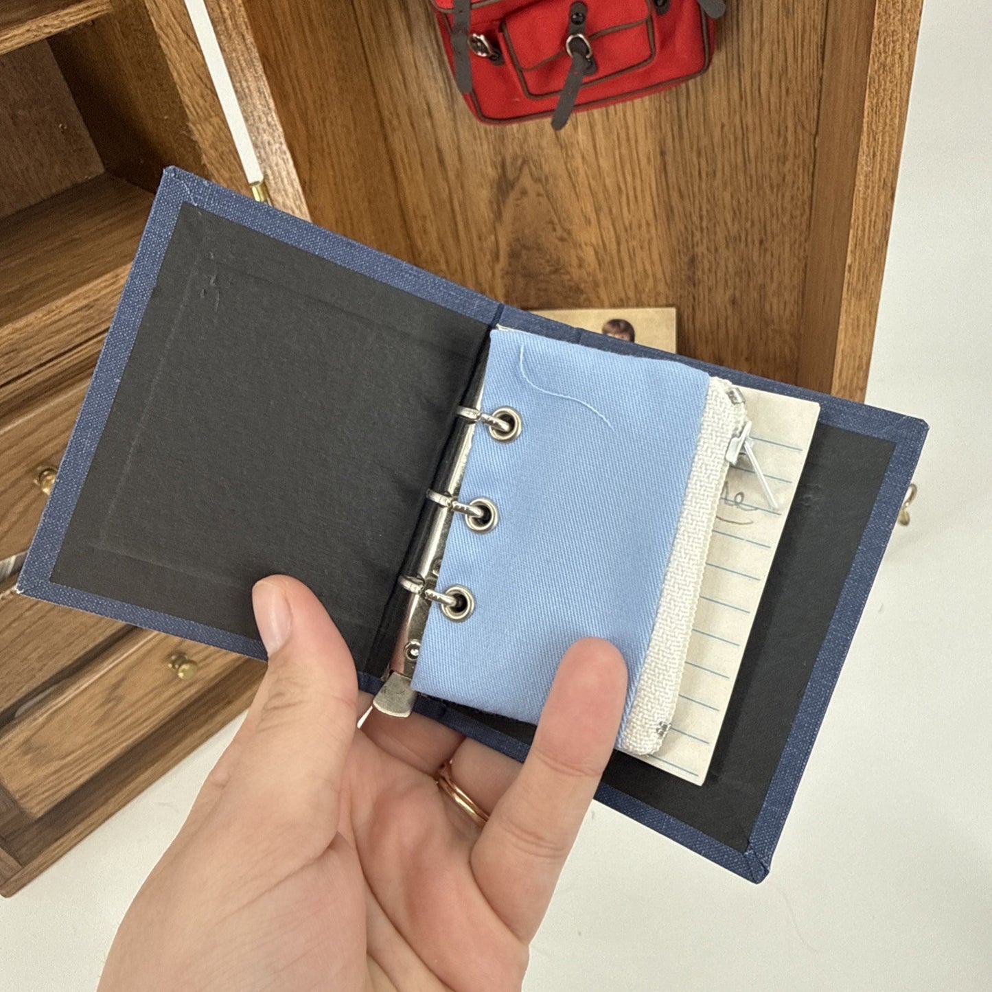 Hand holding a small blue leather-bound notebook with a wooden shelf in the background