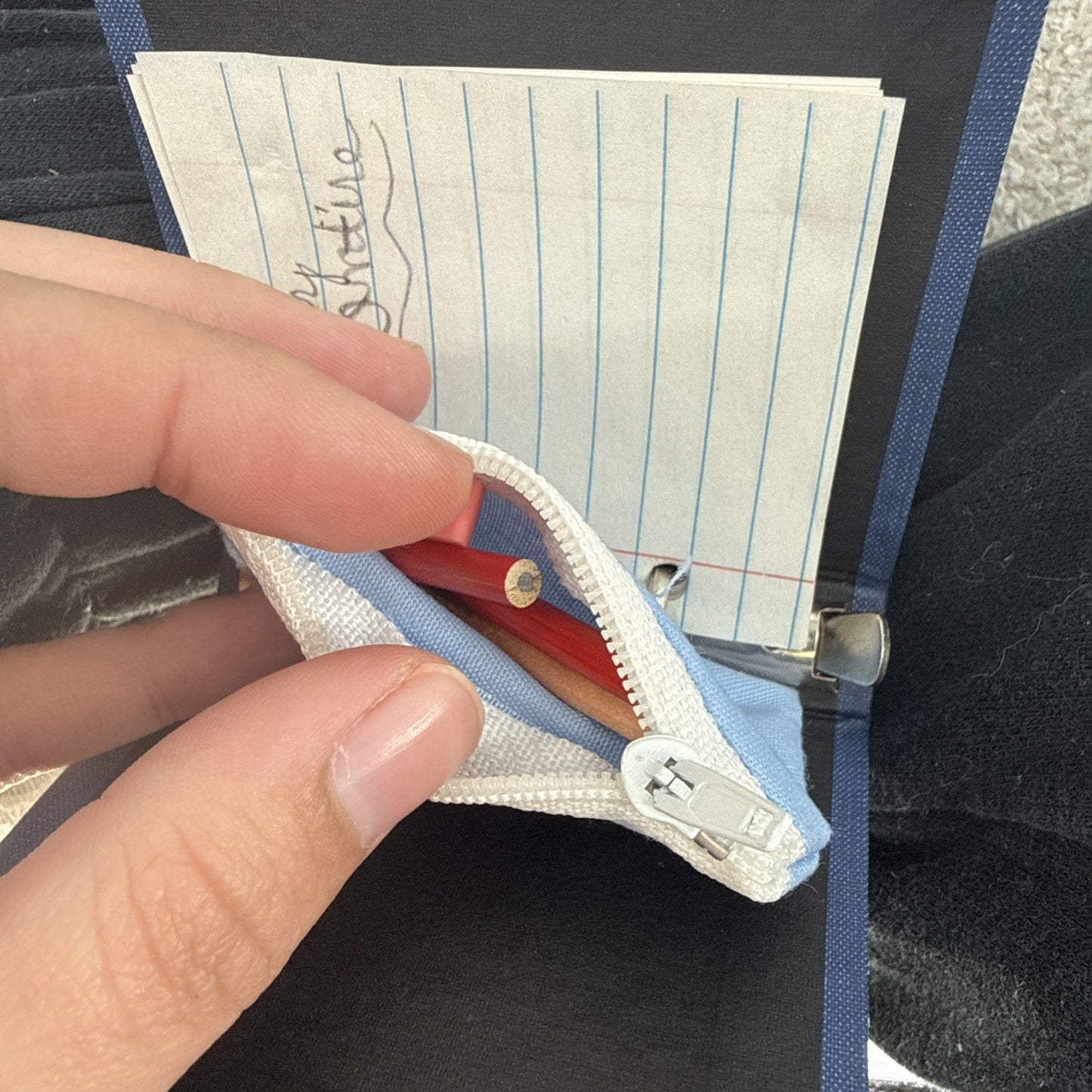Hand opening a small blue pouch with lined paper and a red item inside.