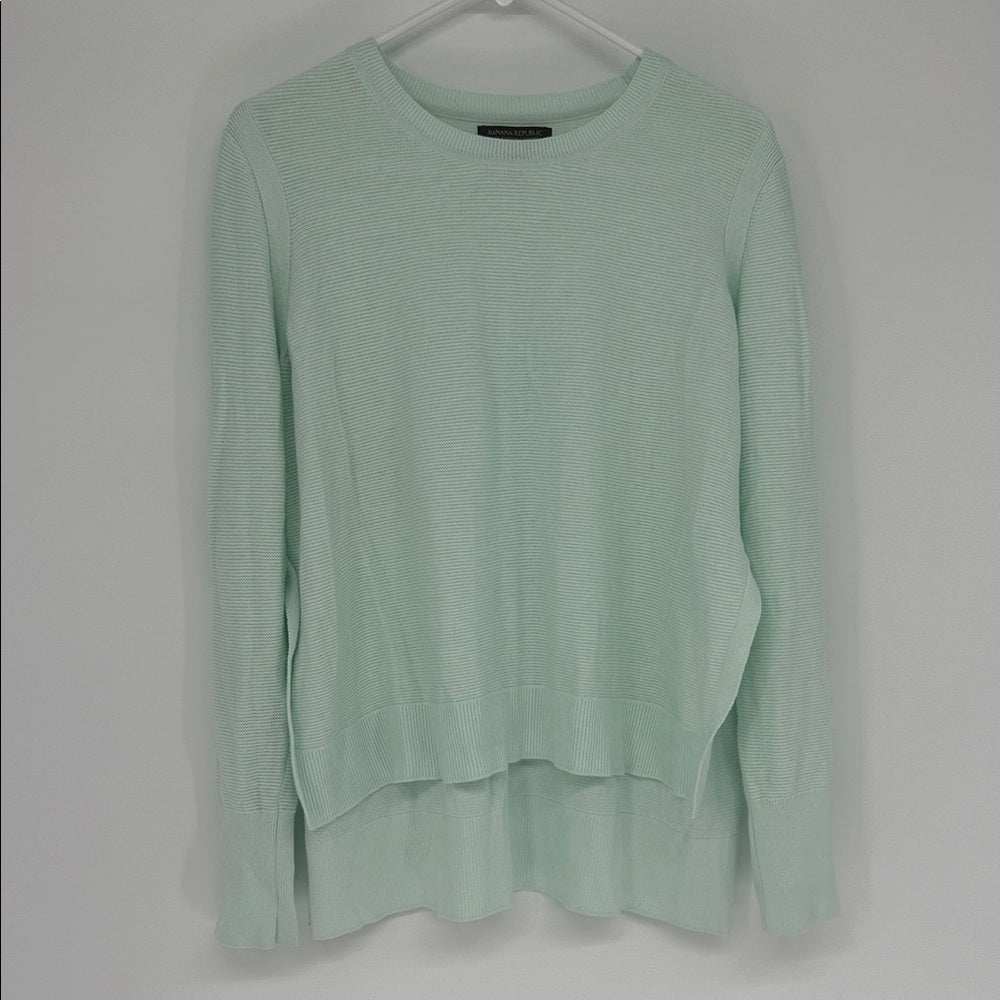 Light green sweater on a hanger against a gray background