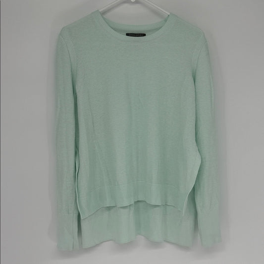 Light green sweater on a hanger against a gray background