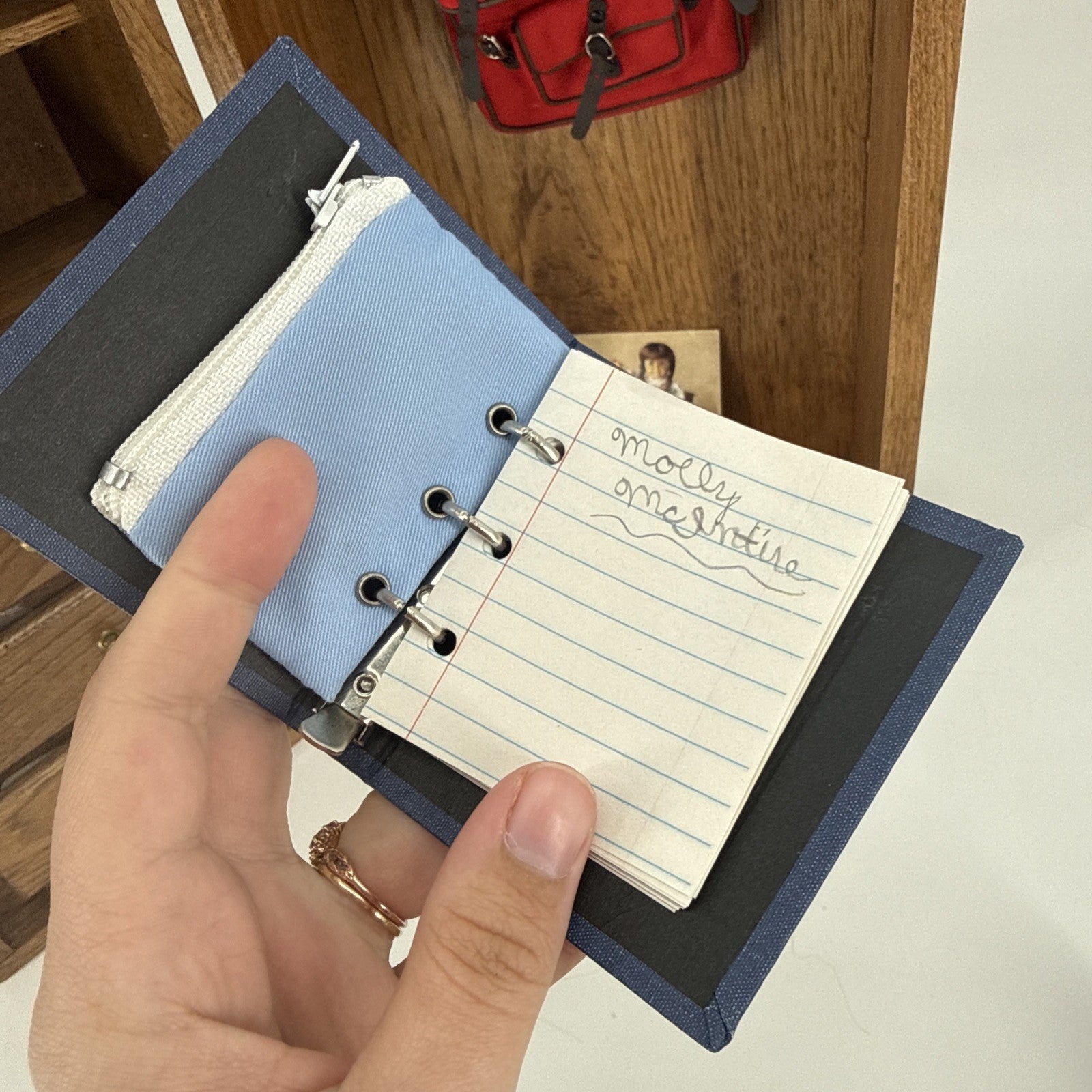 Hand holding a small blue notebook with lined pages on a wooden surface.