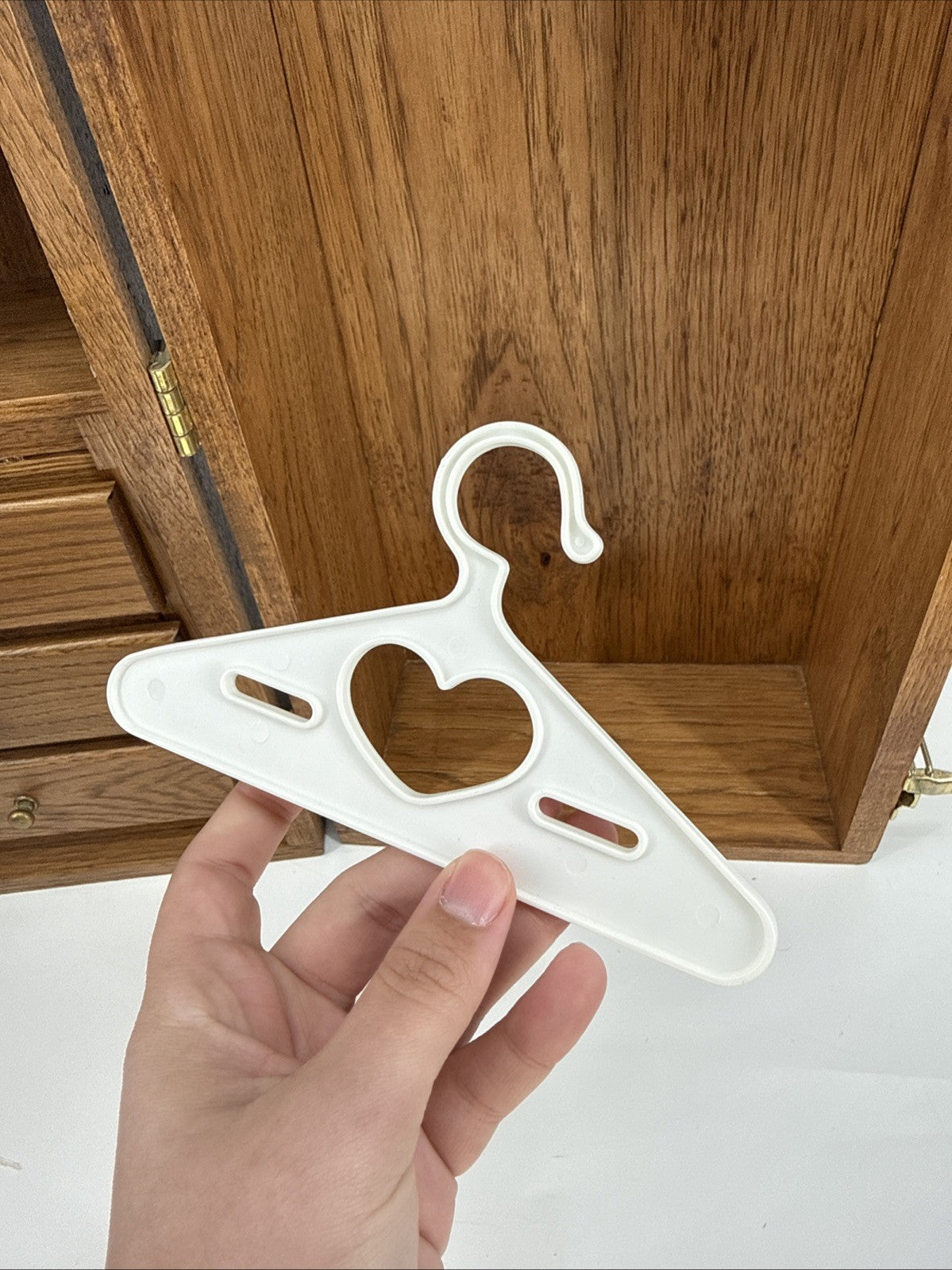 White hanger with heart-shaped hole held by a hand in front of wooden furniture.