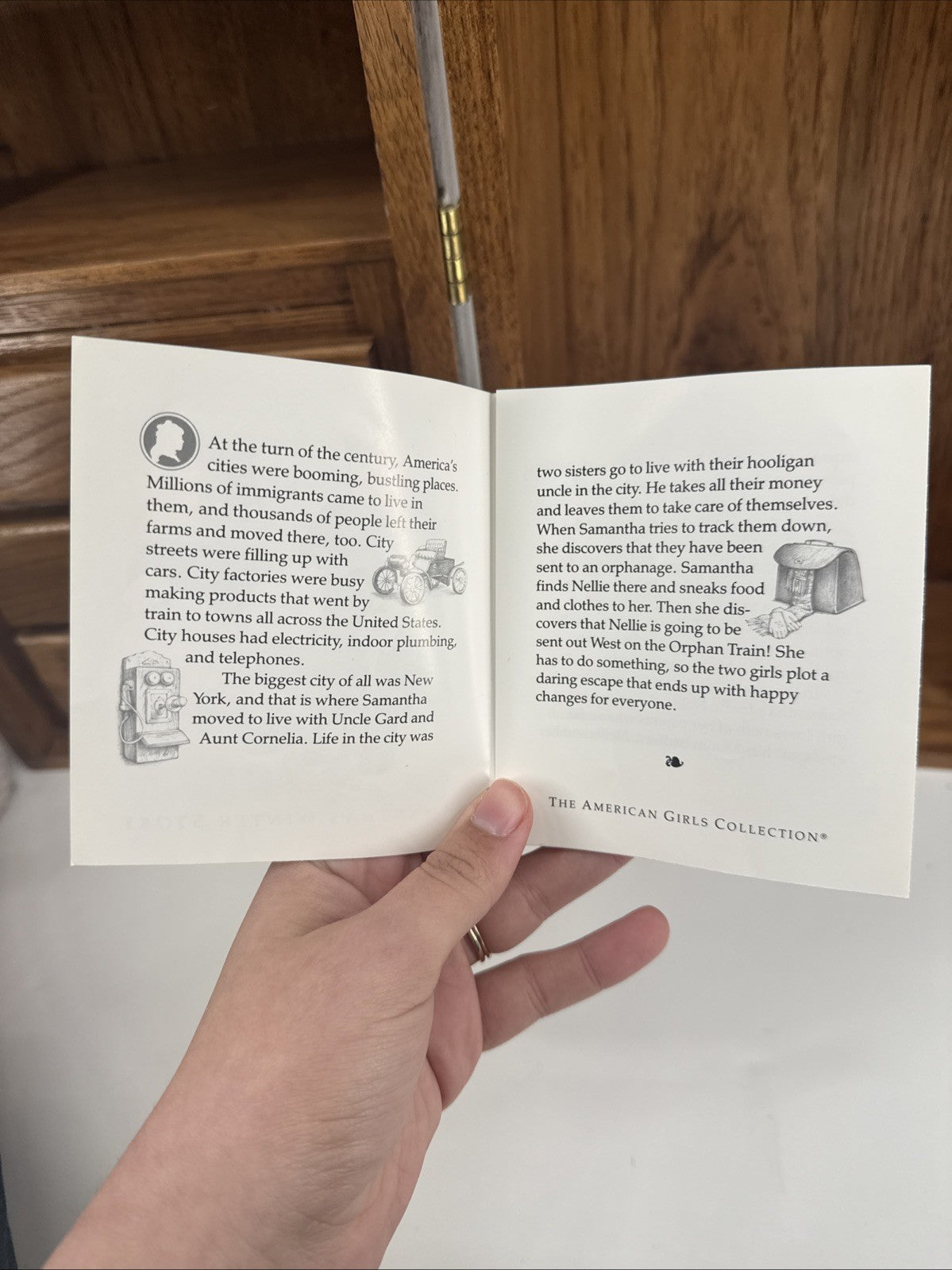 Hand holding an open book with text and illustrations on a wooden surface.