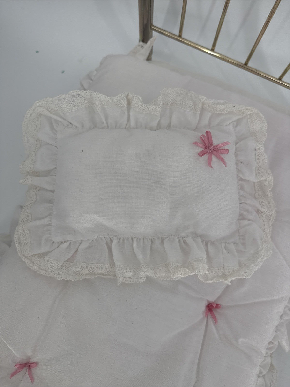 White lace-trimmed pillow with pink flower on a white bedspread.