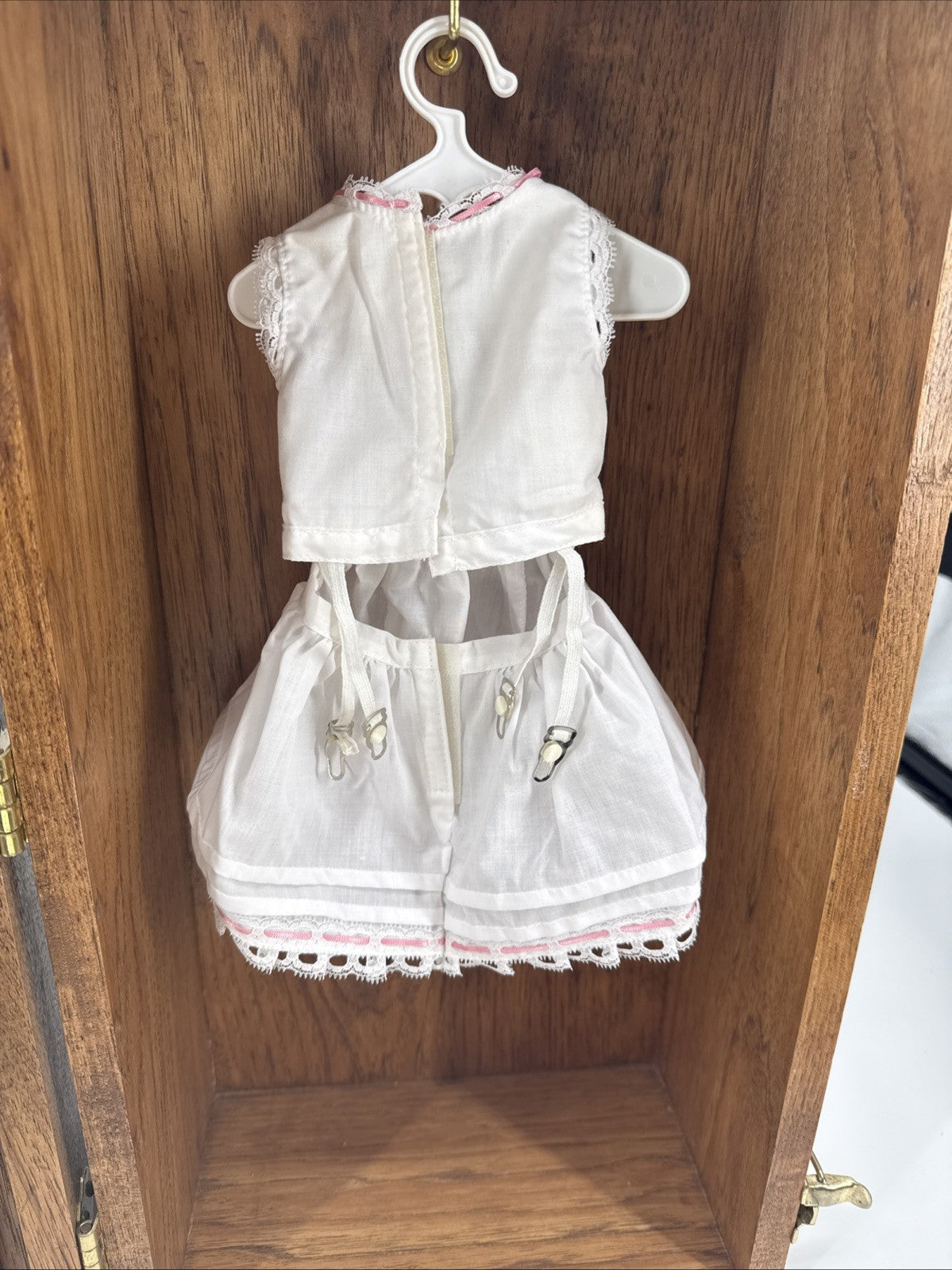White lace dress with pink trim on a hanger against a wooden background