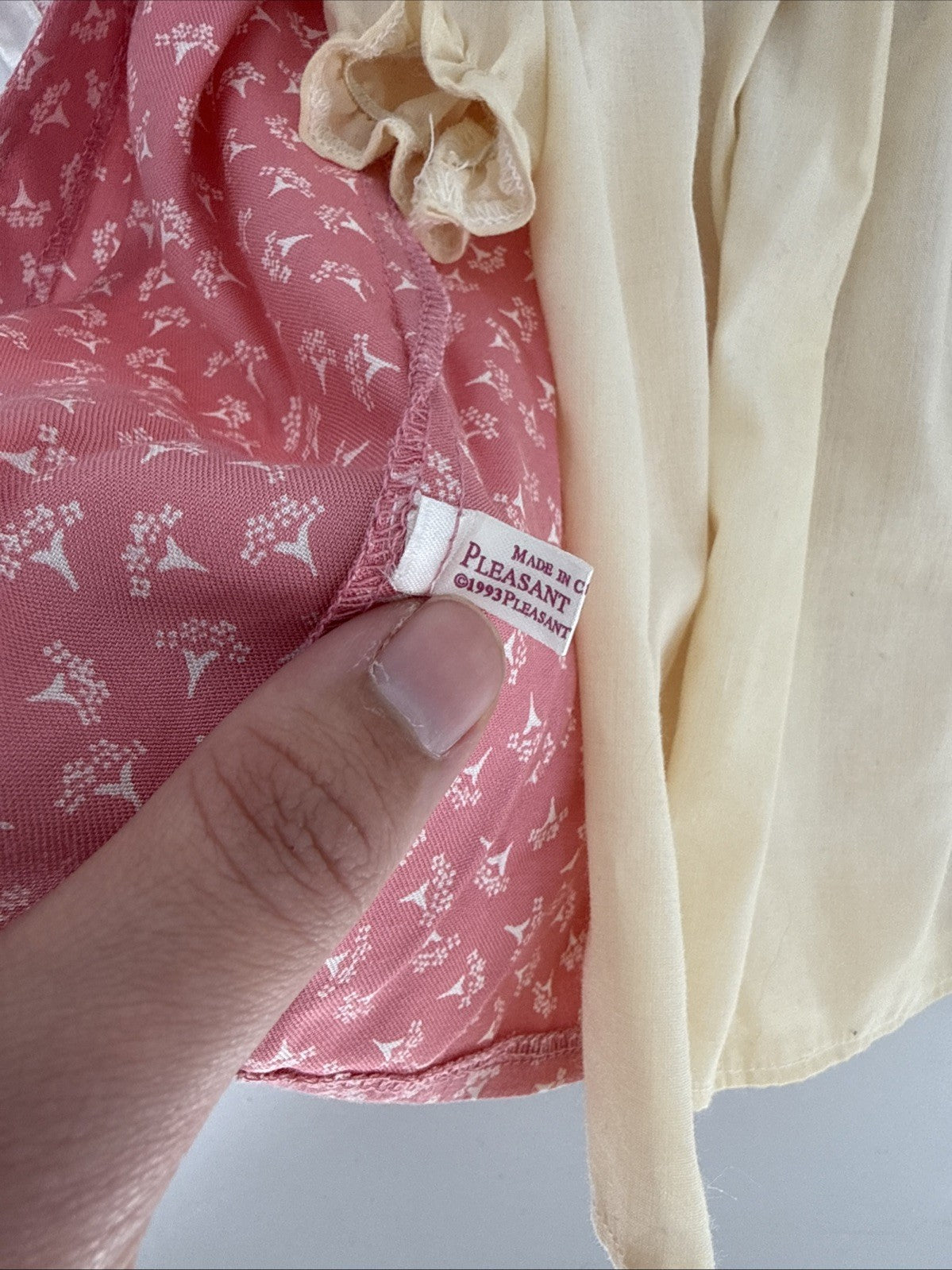 Close-up of a garment with a label, featuring pink fabric with white patterns and beige fabric.
