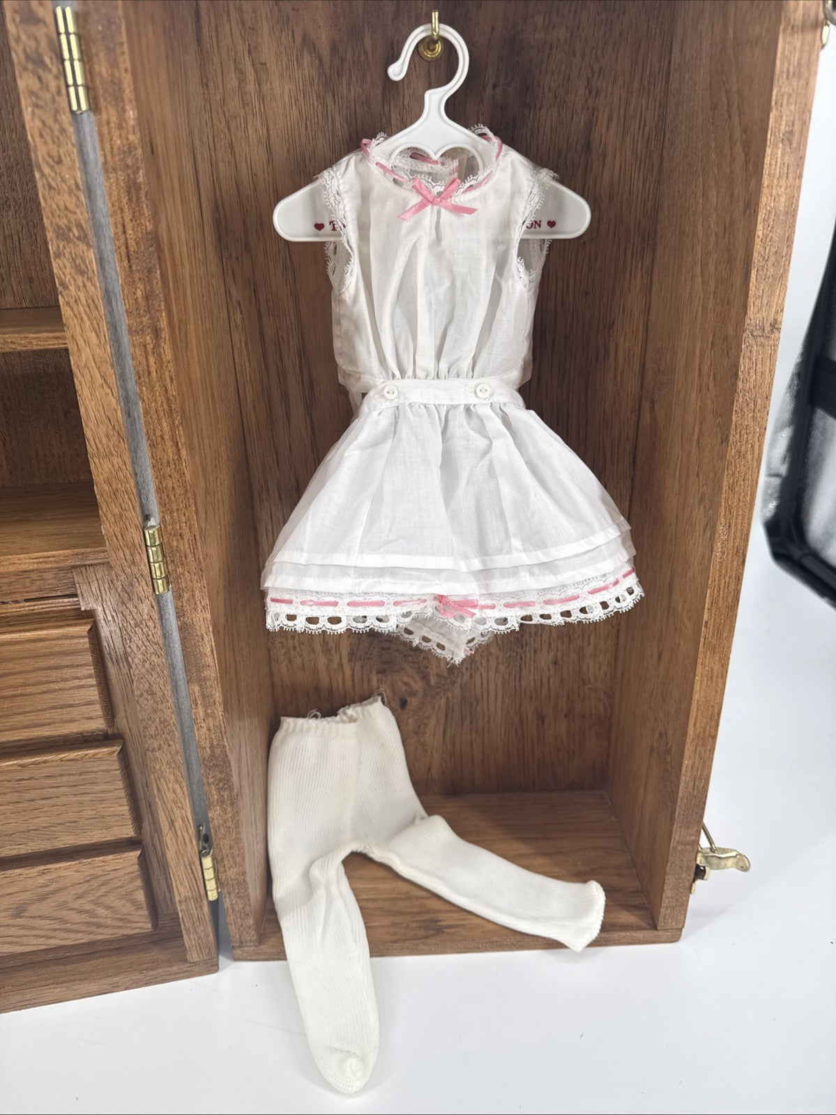 White lace dress with pink accents on a hanger inside an open wooden wardrobe.