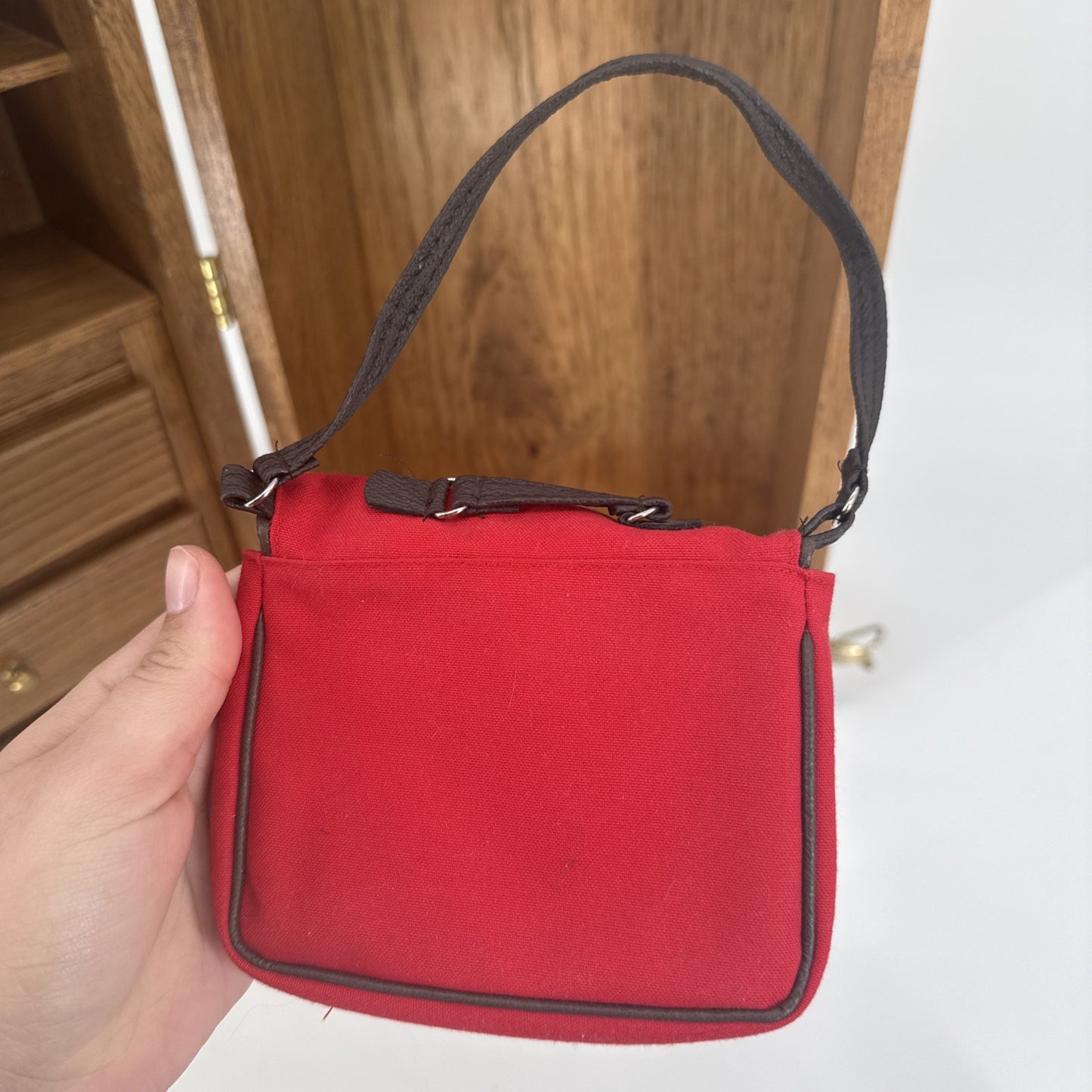 Red handbag with a brown strap held by a hand against a wooden background