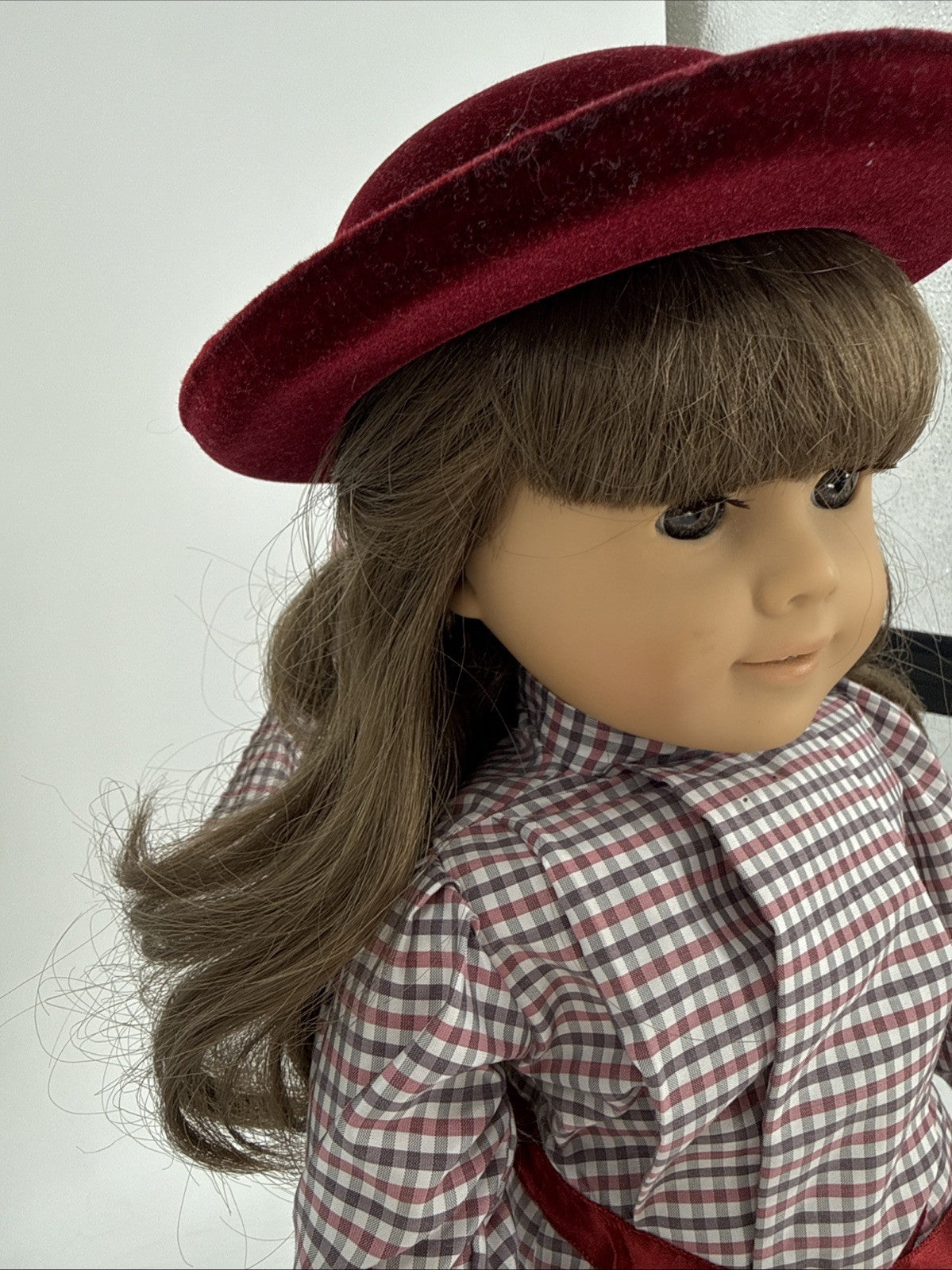 Doll wearing a red hat and checkered shirt against a white background