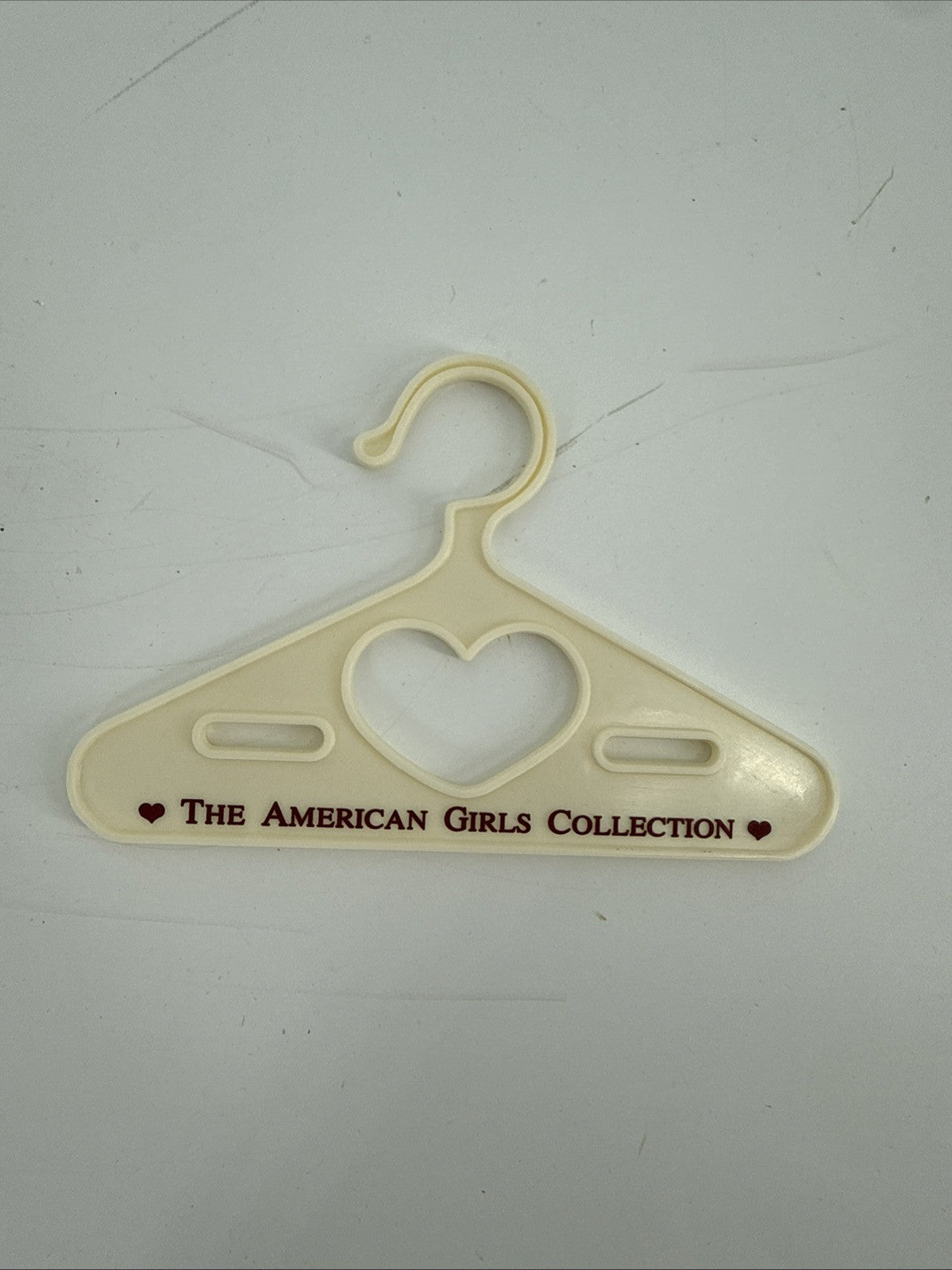 Beige hanger with heart design and 'The American Girls Collection' text on a white background