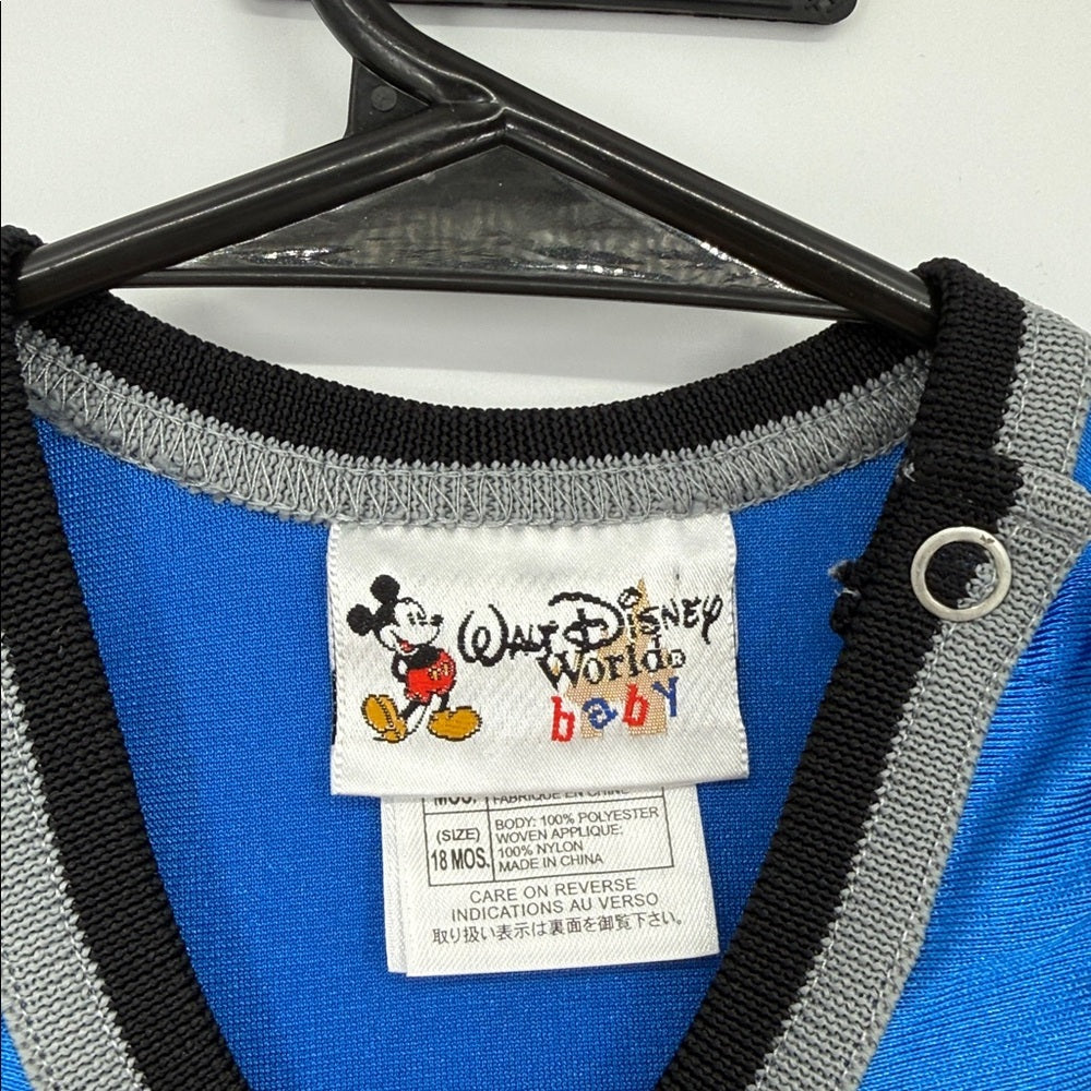 Close-up of Walt Disney World baby label and size tag inside blue Mickey Mouse basketball romper with black and gray trim and shoulder snap detail.