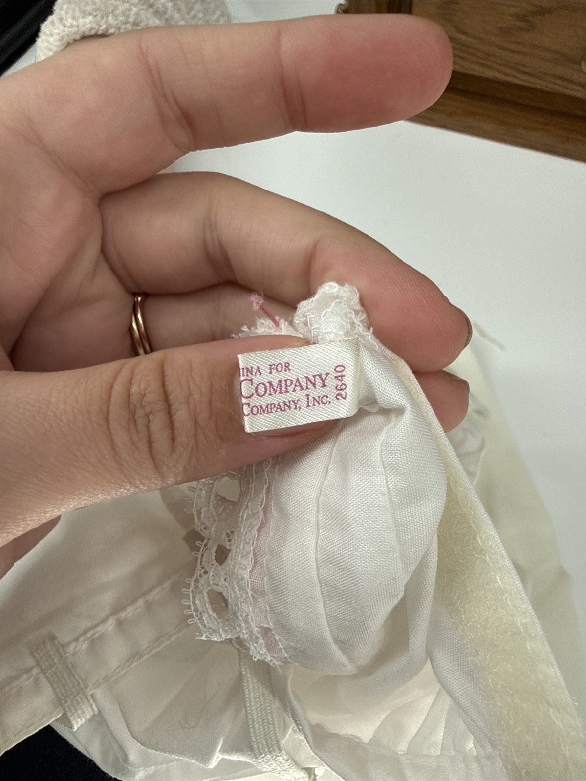 Close-up of a hand holding a white lace garment with a visible label.